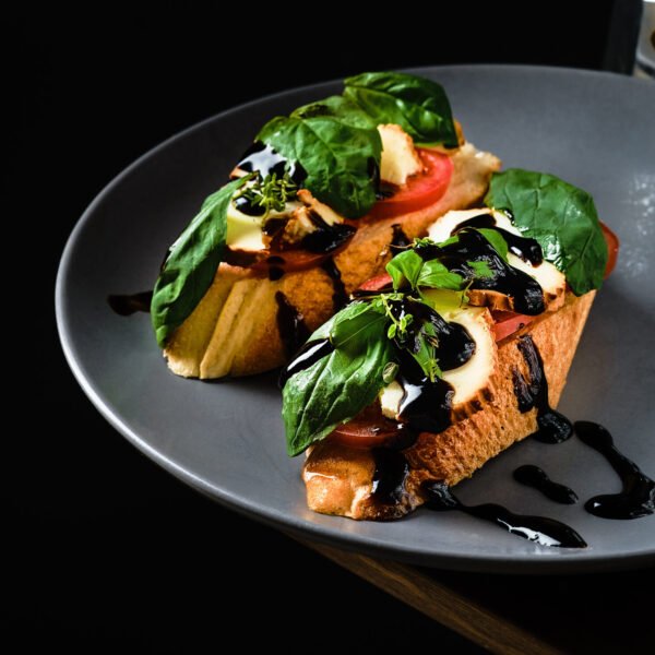 Healthy sandwich on a fresh baguette with basil, tomatoes, grilled cheese and balsamic sauce. Close-up with copy space, coffee pot in the background, breakfast idea